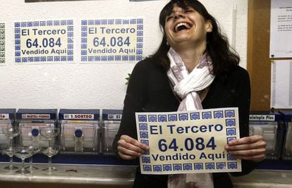 La propietaria de la administraci&oacute;n de Alcal&aacute; de Henares que ha vendido el tercer premio de la Loter&iacute;a de Navidad muestra el n&uacute;mero agraciado, el 64.084, en el interior del establecimiento. 