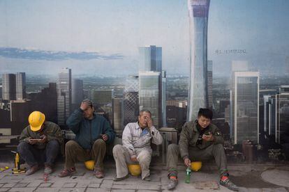 Varios trabajadores de la construcción descansan cerca de un mural con una impresión del Distrito Central de Negocios, en Pekín, China.