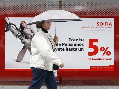 Una mujer camina delante de un cartel que promociona planes de pensiones.