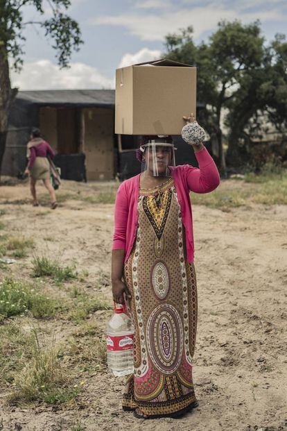 Una mujer de Nigeria porta una caja de alimentos, agua y equipos de protección contra la COVID 19 donados por distintas entidades sociales y ONG en un asentamiento de temporeros en Lucena del Puerto (Huelva).