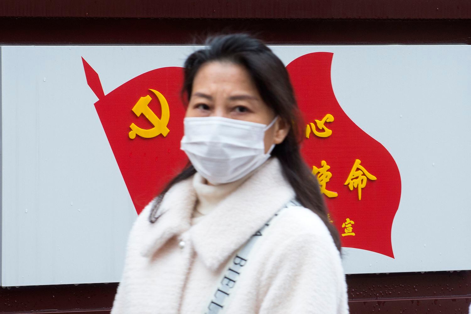 Una mujer pasa delante de una bandera del Partido Comunista