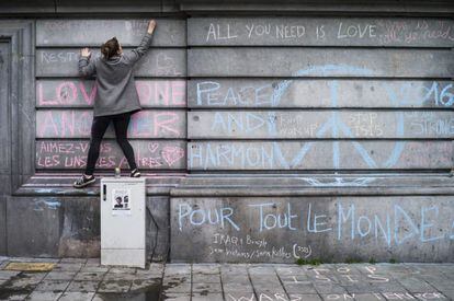 Una joven escribe, ayer, un mensaje en recuerdo de las víctimas de los atentados terroristas en un muro de la Plaza de la Bolsa de Bruselas.