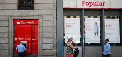 FILE PHOTO: A man uses a cash dispenser at a Santander branch next to a Banco Popular branch in Madrid, Spain.