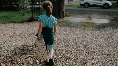 Image depicting transportation of a child to school. A little girl in a school uniform walks across a driveway towards a waiting car on the road.