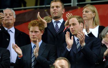 Los príncipes Harry (segundo por la izquierda) y Guillermo de Inglaterra (a su lado), aplauden con cara seria a su selección en el partido contra Argelia.