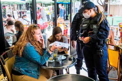 Una agente controla que los clientes de un bar en París poseen el certificado covid.