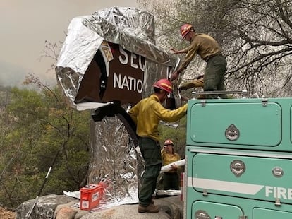 Tres bomberos cubren un cartel de madera con aluminio, este viernes en California.