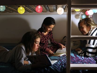 Dos niñas de nueve y 11 años leen un libro con su madre en su casa.