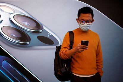 Un joven consulta su iPhone 12 frente a una tienda de Apple en Shanghái.