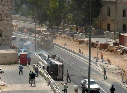 El autobús de pasajeros volcado por el impacto de una excavadora (detrás), en la céntrica calle de Yaffa, en Jerusalén.