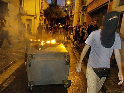 Un joven encapuchado junto a un contenedor ardiendo, anoche, en las calles de Sants.