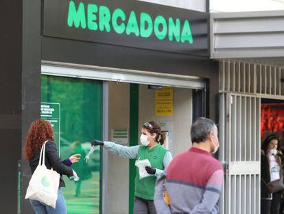 Una trabajadora de un supermercado da guantes a las decenas de personas que esperan una larga cola, en Madrid. 