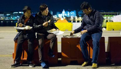 Tres jóvenes cenan las raciones que se distribuyen a los refugiados en el Puerto del Pireo, Atenas.