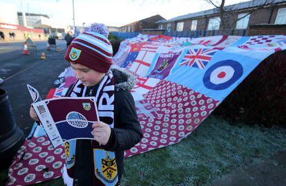 Un niño examina el programa del partido del Burnley FC contra el Leicester City frente a un simpático mural de expresión nacionalista
