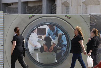 Dos mujeres pasean por delante de un cartel utilizado para cubrir obras en el hospital Virgen del Rocío.