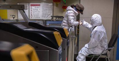 Trabajador del metro de Wuhan, con un traje de protección, da indicaciones a una viajera.