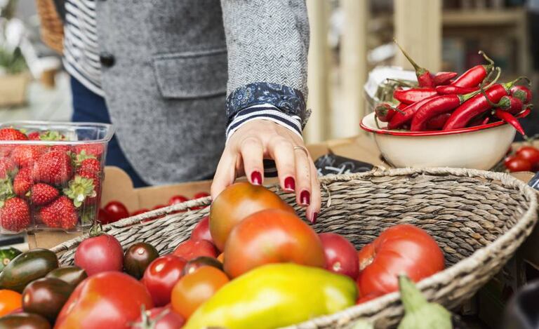 Una mujer coge un tomate de una cesta de verduras.