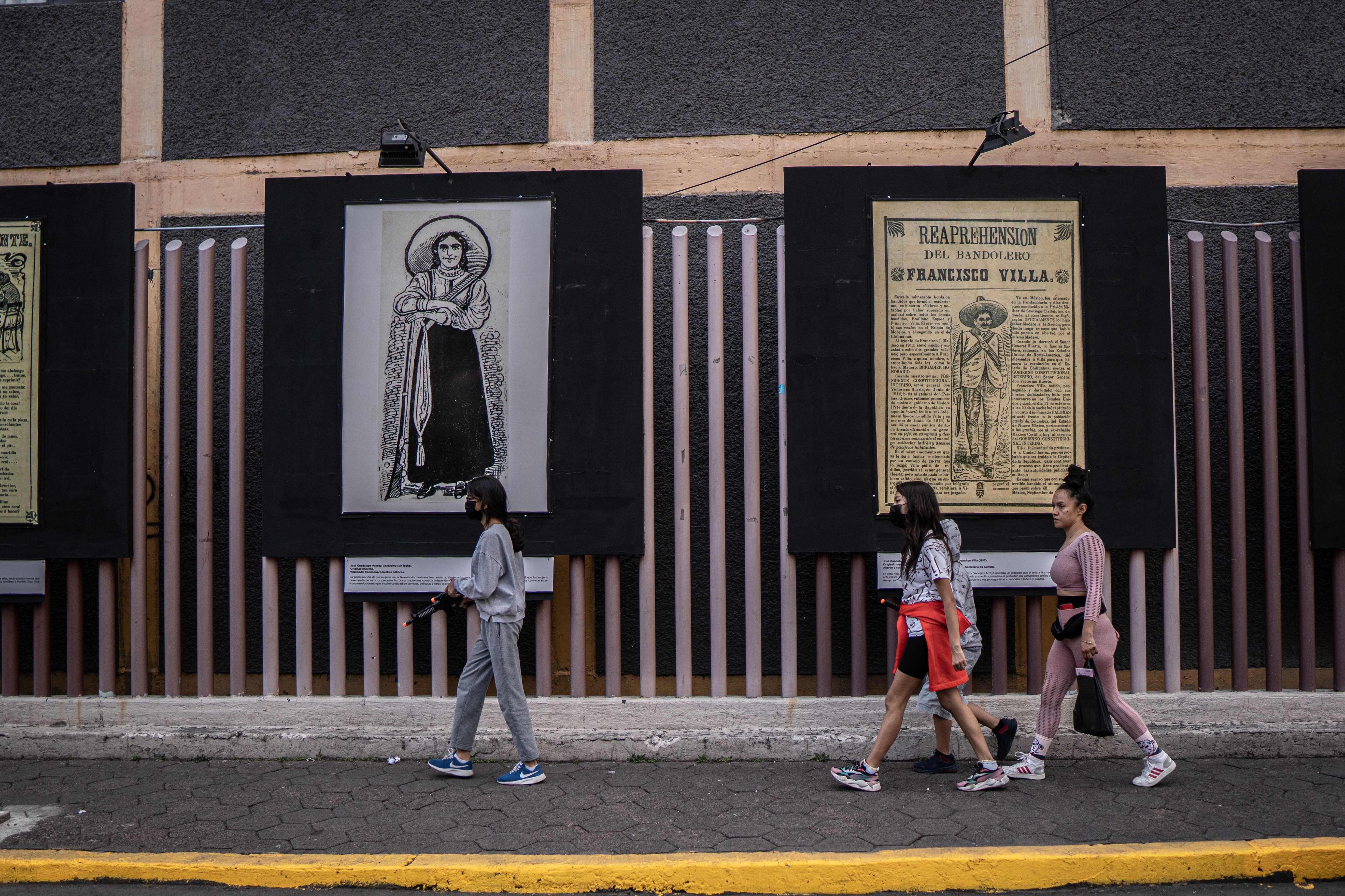 Transeúntes al lado de la exposición de José Guadalupe Posada en la calle ayuntamiento de la delegación Iztapalapa.