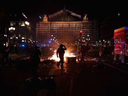 Un policía y un bombero, ante un contenedor de basura en llamas ante el edificio de la ópera de de París, durante una manifestación este 20 de marzo.