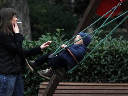 Una mujer fuma un cigarrillo ante un columpio ocupado por un niño en el parque del Retiro de Madrid