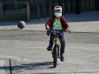 Un niño monta en bici con una mascarilla en Pekín.