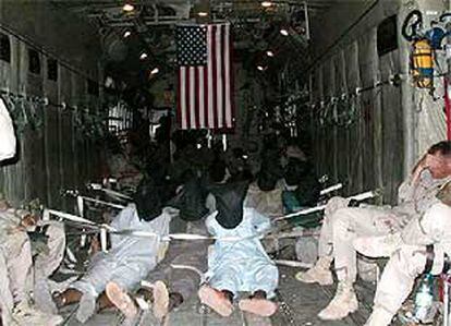 Los presos yacen tumbados, atados y encapuchados bajo la vigilancia de soldados norteamericanos.