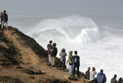 La gente mira desde un acantilado mientras varios surfistas practican Tow. in en la enormes olas de Nazaré. 