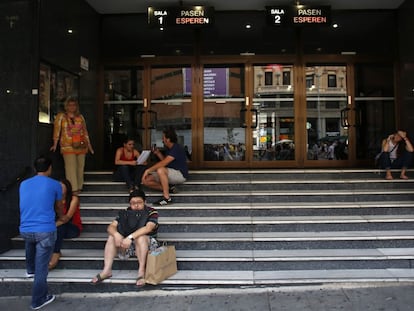 Varias personas descansan en las escaleras de un cine en la Gran Vía, en Madrid.