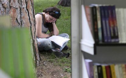 Una mujer lee un libro sentada en el c&eacute;sped, junto a las casetas de la Feria del Libro de Madrid, en el madrile&ntilde;o parque del Retiro.