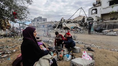 Una familia se reúne alrededor del fuego frente los escombros de su casa, destrozada por los ataques israelíes, este martes en Jan Yunis.