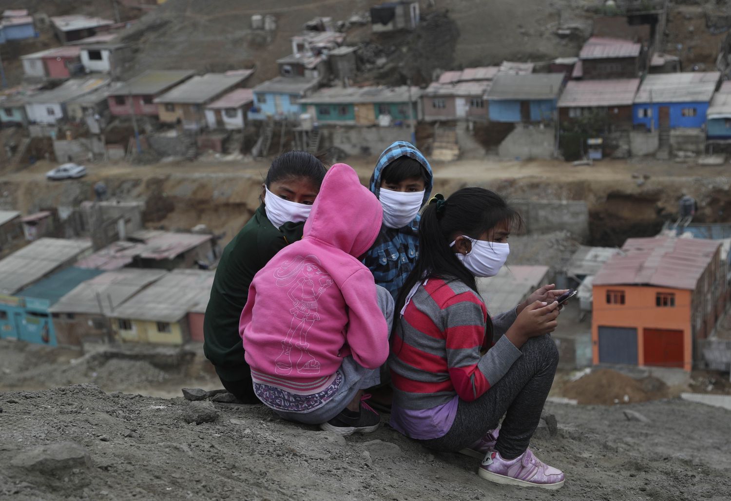 Niños con máscaras para prevenir la propagación del nuevo coronavirus, reciben clases virtuales a través de sus teléfonos móviles sentados en lo alto de una colina en el barrio de Puente Piedra, en las afueras de Lima, Perú.