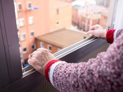 Una anciana se asoma por la ventana de un piso alto en la ciudad.