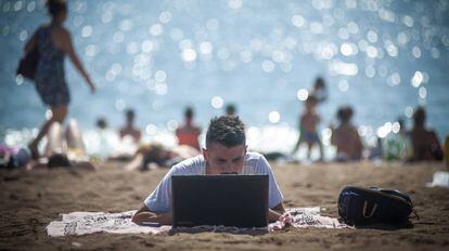Una persona utiliza su ordenador en la playa de la Barceloneta.