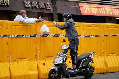 Un hombre entrega comida a otro a través del muro que separa las dos mitades de Shanghái a causa del confinamiento.