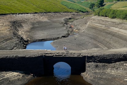 Dos personas caminan por la tierra seca que antes cubría el agua en el embalse de Ripponden, este viernes.
