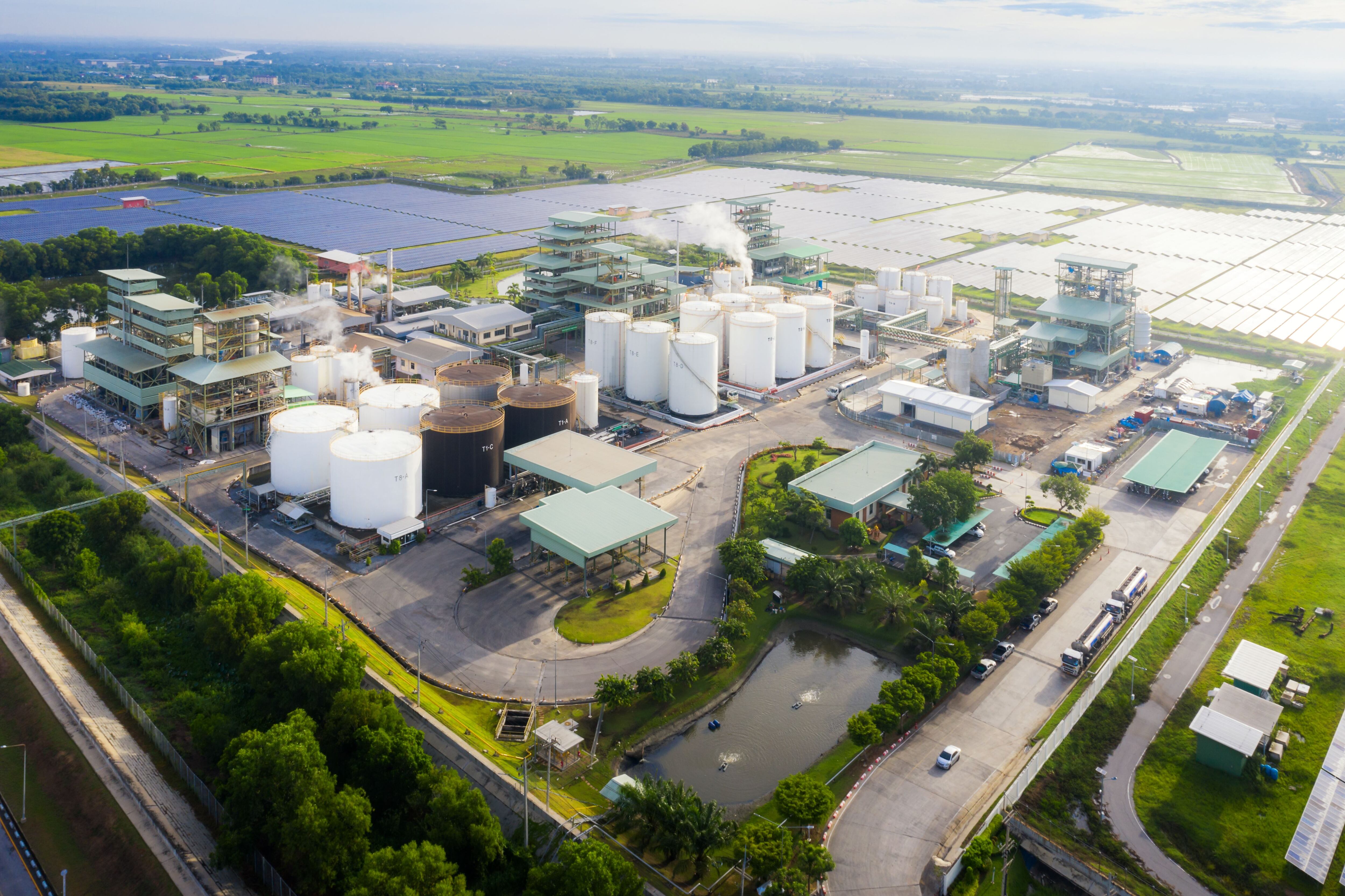 Foto aérea de una zona industrial que muestra una refinería de petróleo con tanques de almacenamiento junto a una estación de energía solar para suministro de energía renovable.