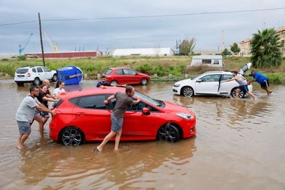 Varias personas arrastran sus coches afectados por la tromba de agua en Puerto de Sagunto.