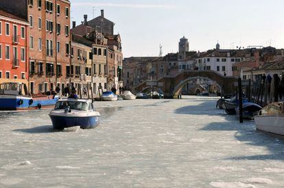Un barco navega por un canal de Venecia cubierto de hielo.