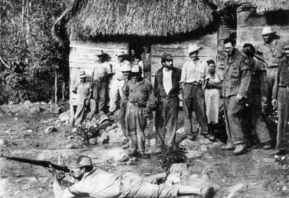 Fidel Castro, a la derecha de la imagen con gafas, contempla a un guerrillero mientras hace ejercicios de tiro tendido en el suelo, con varios guerrilleros más observando la escena, tomada en Sierra Maestra en fecha sin determinar.