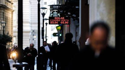 Personas caminan junto a una pizarra con el valor del dólar en Buenos Aires.