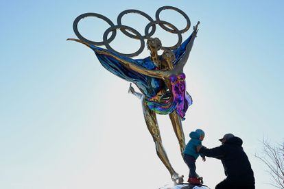 A man plays with a child next to a sculpture with the Olympic rings in Shougang Park in Beijing on Tuesday.