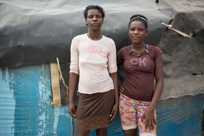 Tamena Simple, de 22 años (derecha), junto a su madre, Ana Yedi, de 40 años, frente a su vivienda en el campamento fronterizo de desplazados, Parc Cadeau I. Los desplazados construyeron sus viviendas con los materiales que tenían a mano. 

