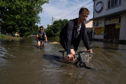 Dos personas intentan cruzar en bicileta una calle inundada de Jersón, este martes.