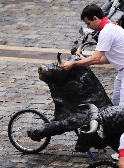 Un hombre empuja uno de los toros ficticios que corren en el 'encierro txiki' de Sanfermines.