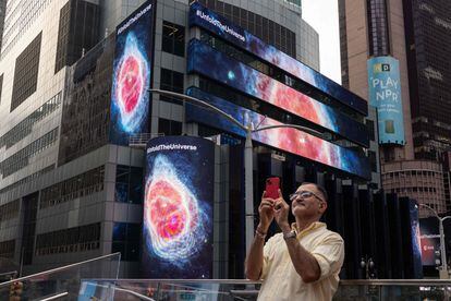 Un hombre fotografía las imágenes de una nebulosa obtenidas con el James Webb en Times Square, Nueva York.