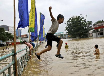 Un niño indonesio se lanza al agua mientras juega en una parte inundada de la ciudad de Yakarta, Indonesia