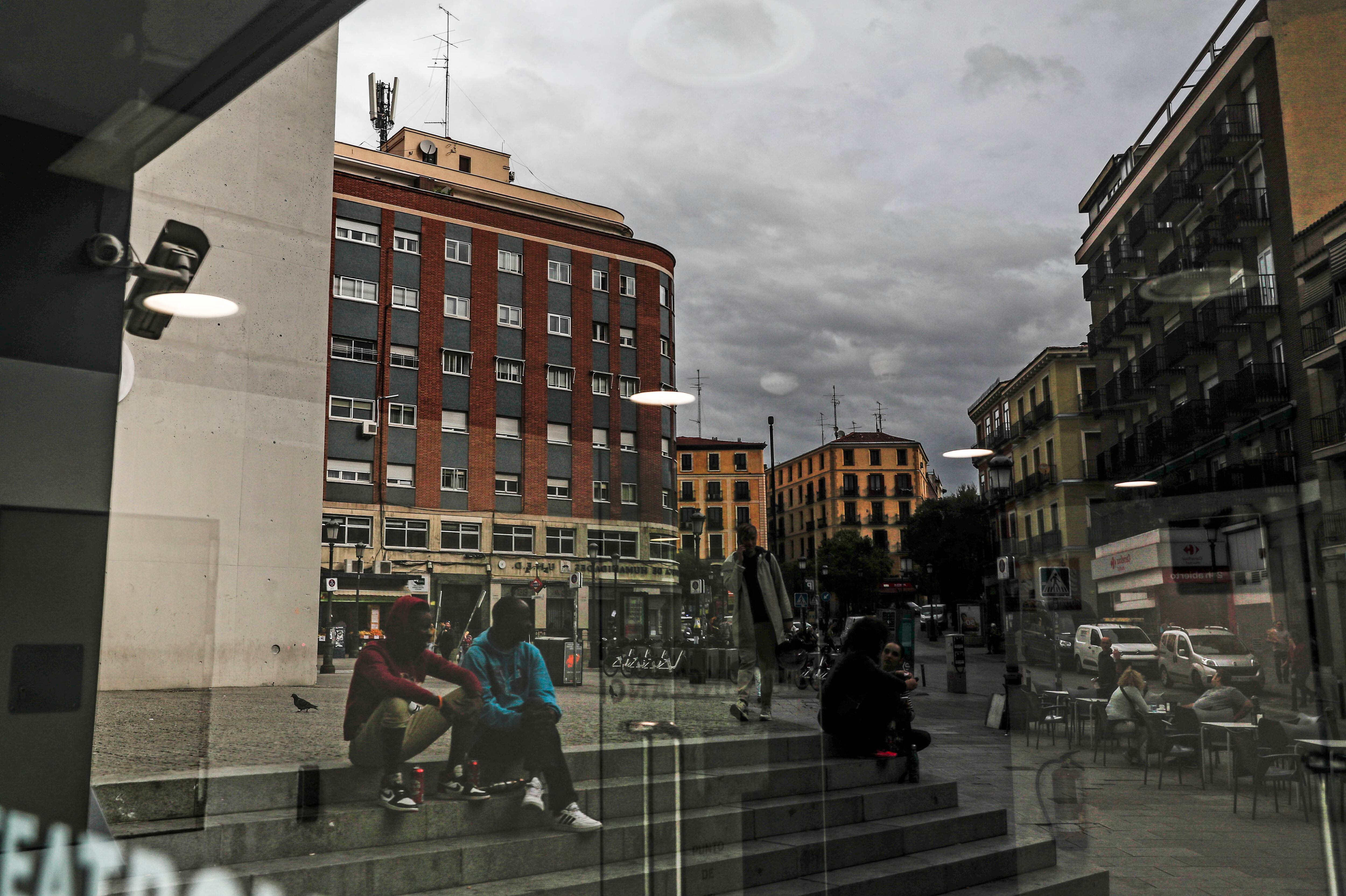 Varias personas se reflejan en un escaparate en la plaza Lavapiés. 