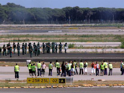 En primer término, los trabajadores de Iberia ocupan, el viernes pasado, las pistas de El Prat. Al fondo, agentes antidisturbios de la Guardia Civil.