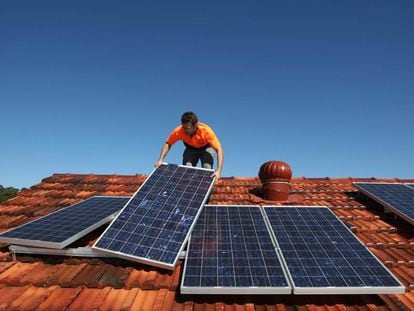 Un operario coloca paneles solares en el tejado de una casa.