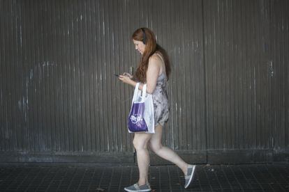 Una dona camina mirant el mòbil amb els auriculars posats.
